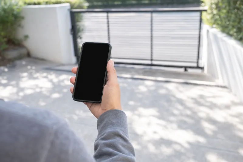 Una mano con lo smartphone davanti al cancello.